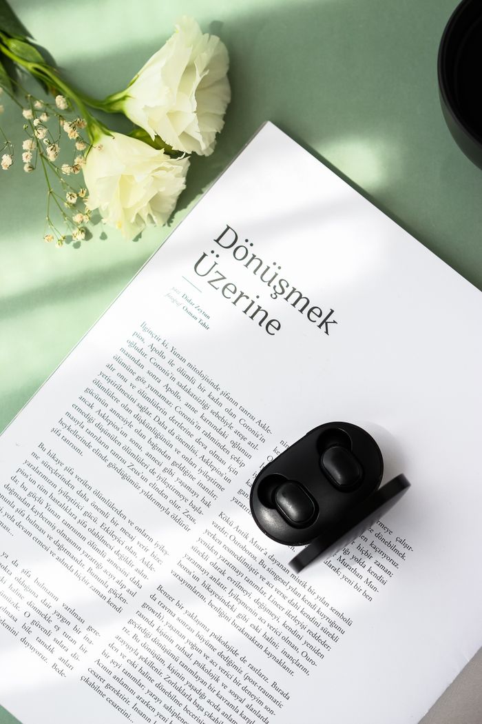 A minimalist composition featuring earbuds on a journal with white flowers, creating a serene still life.